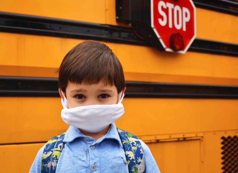 Child with mask in front of school bus