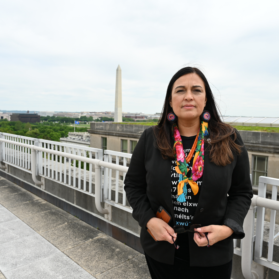 NABS CEO Deborah Parker in Washington, D.C. with the Washington monument in the background. Parker wears an orange kokum scarf around her neck, earrings, and a somber expression.